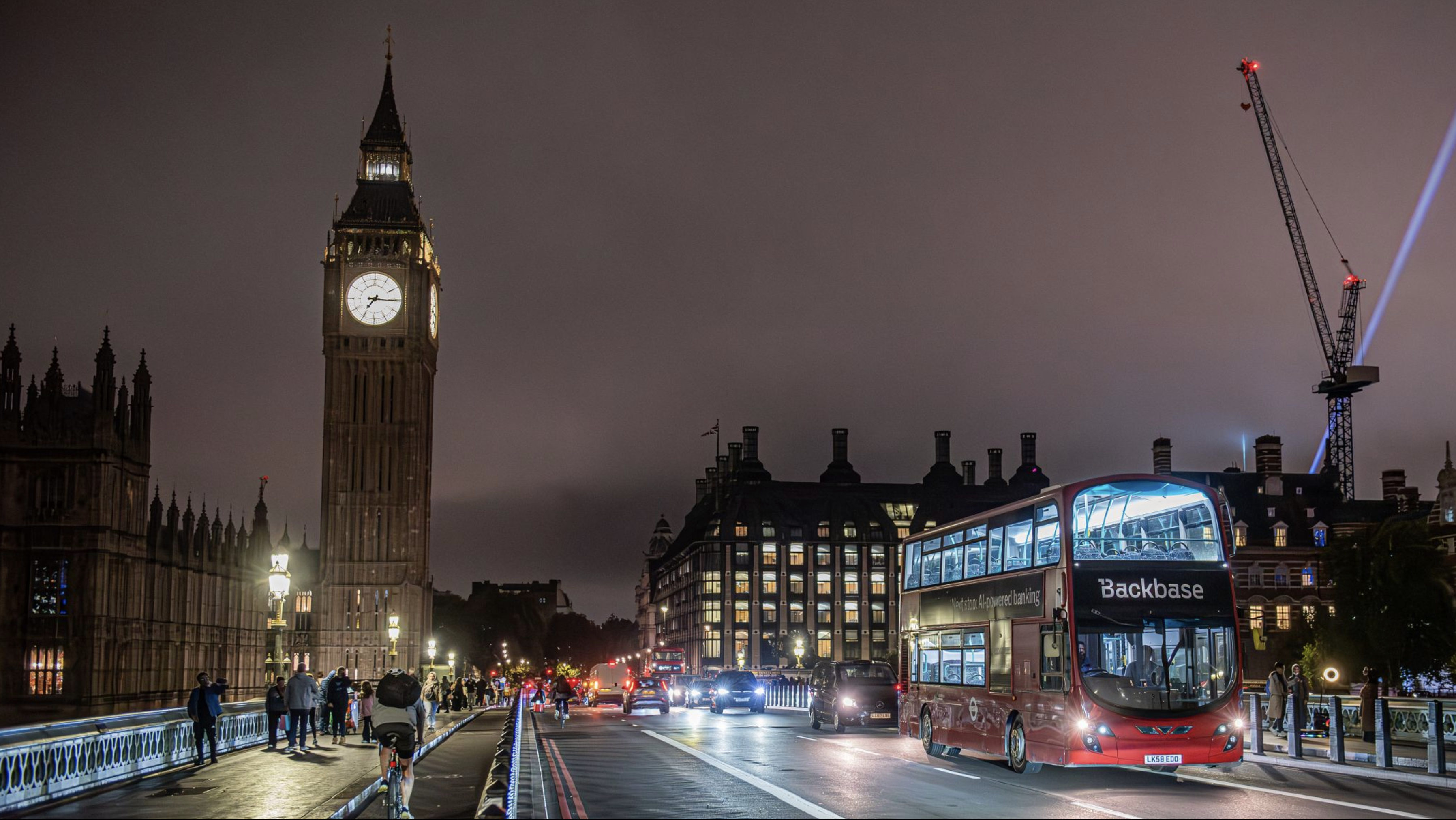 Backbase-branded double-decker bus crossing Westminster Bridge at night with Big Ben in the background